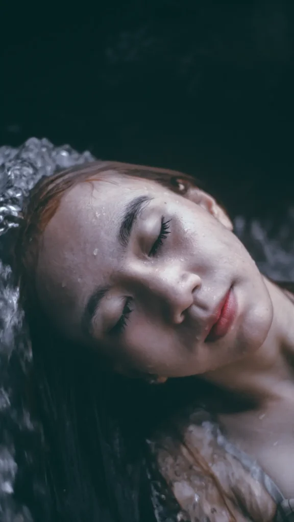Woman resting peacefully in dark teal water with eyes closed, representing renewal